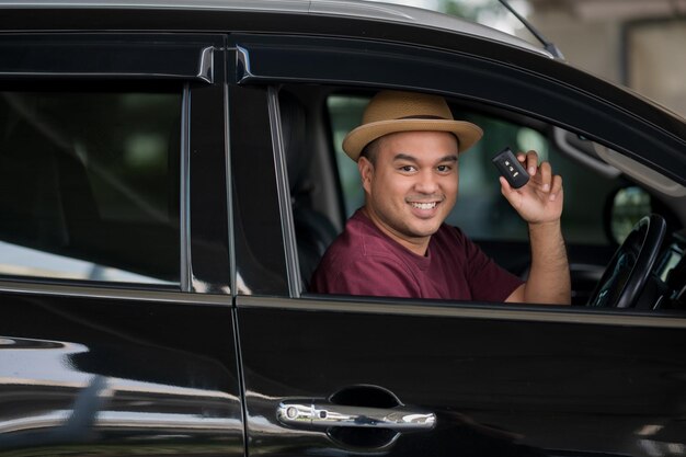 Jovem bonito asiático recebendo o carro novo. ele está mostrando a chave do carro e muito feliz. compre ou alugue um conceito de carro.