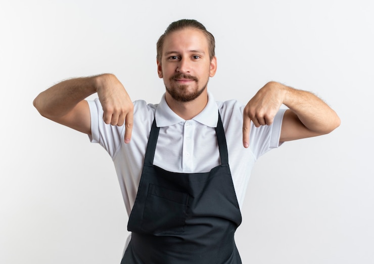 Foto grátis jovem bonito barbeiro satisfeito vestindo uniforme apontando para baixo, isolado na parede branca