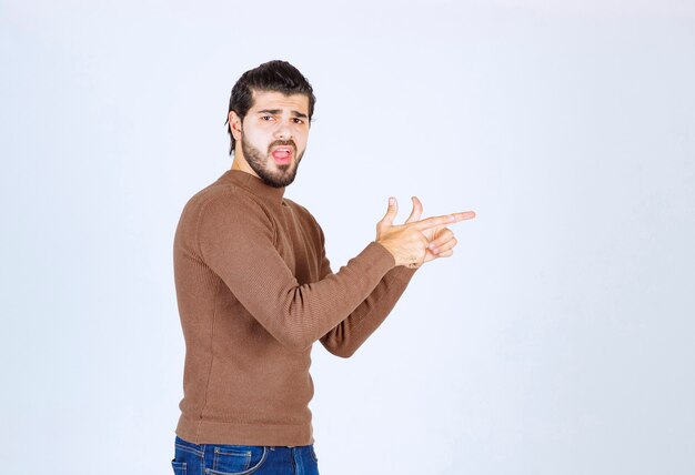 Jovem bonito barbudo apontando para longe no fundo branco cinza. Foto de alta qualidade