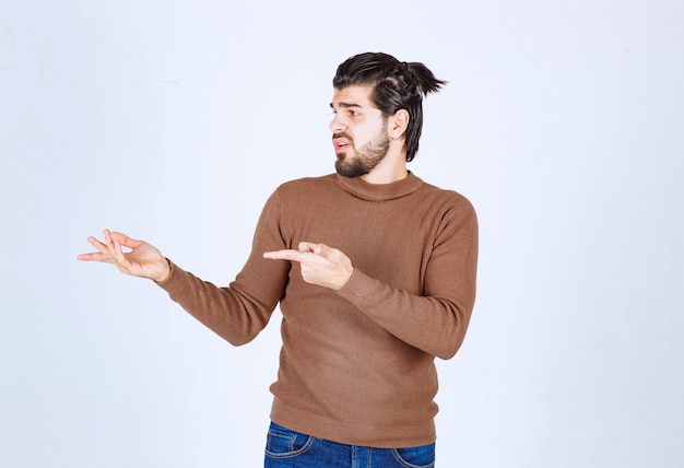 Jovem bonito barbudo apontando para longe no fundo branco cinza. foto de alta qualidade