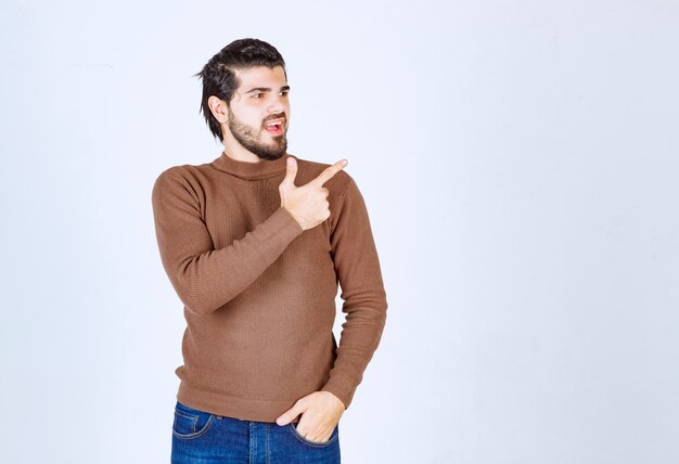 Jovem bonito barbudo apontando para longe no fundo branco cinza. Foto de alta qualidade