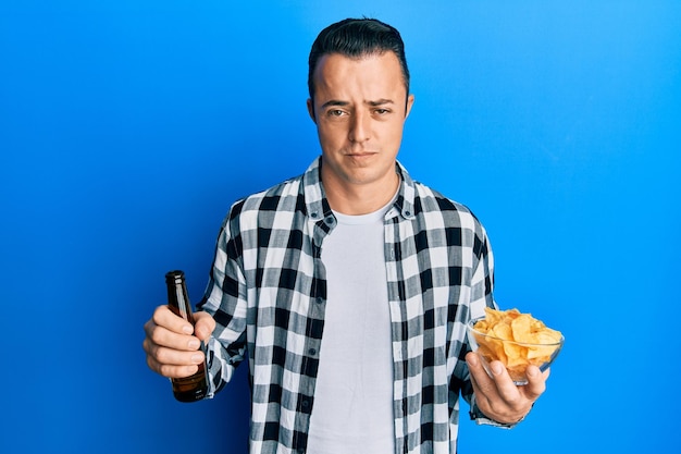 Foto grátis jovem bonito bebendo um litro de cerveja segurando batatas fritas cético e nervoso franzindo a testa chateado por causa do problema pessoa negativa