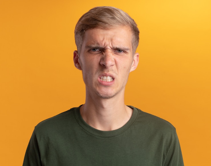 Foto grátis jovem bonito carrancudo vestindo uma camisa verde isolada na parede amarela