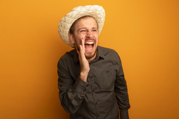 Jovem bonito com camisa cinza e chapéu de verão gritando ou chamando alguém de emocional e animado
