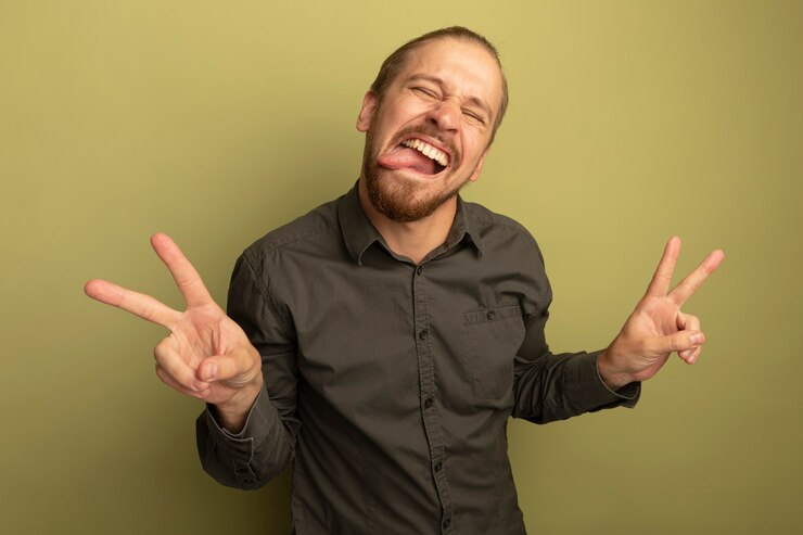 Foto grátis jovem bonito com camisa cinza feliz e animado, mostrando a língua e mostrando o sinal v