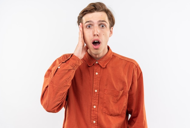 Jovem bonito com medo de camisa vermelha colocando a mão na bochecha