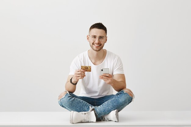 Jovem bonito com óculos, posando com seu telefone e cartão