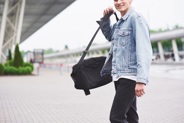 Jovem bonito com uma bolsa no ombro com pressa para o aeroporto.