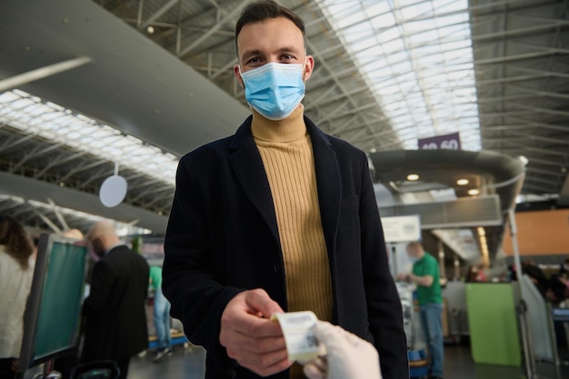 Jovem bonito com uma máscara médica protetora recebe um código qr após ser testado antes da partida no aeroporto internacional. voo seguro e viagens durante uma pandemia