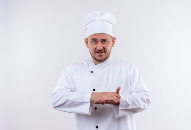 Jovem bonito cozinheiro satisfeito em uniforme de chef, mantendo as mãos juntas isoladas no espaço em branco