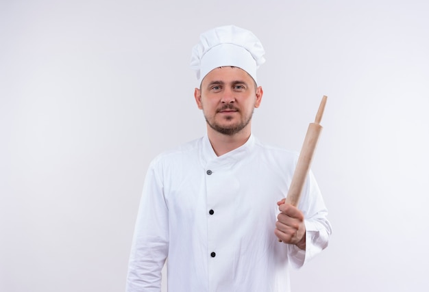 Jovem bonito cozinheiro satisfeito em uniforme de chef segurando o rolo de massa isolado no espaço em branco