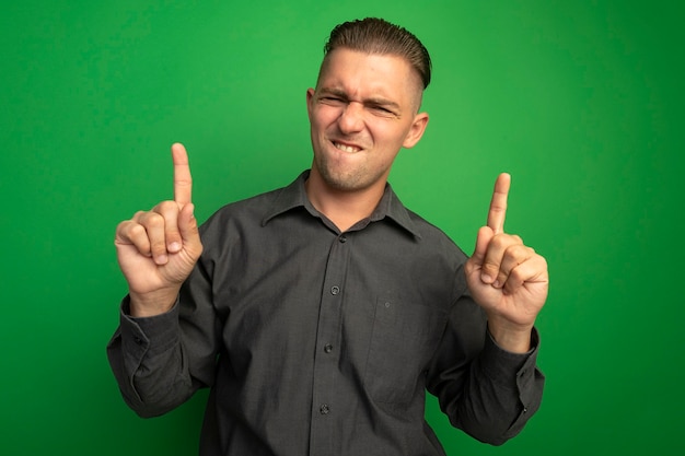 Jovem bonito de camisa cinza parecendo confiante e feliz mostrando os dedos indicadores