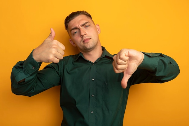 Foto grátis jovem bonito de camisa verde com expressão cética mostrando os polegares para cima e para baixo