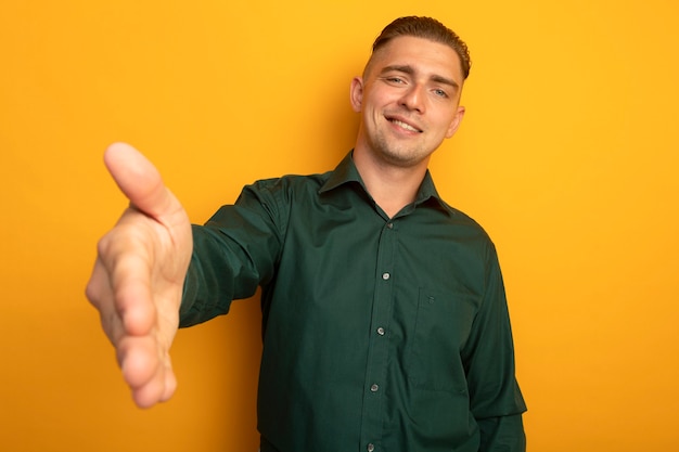 Jovem bonito de camisa verde oferecendo saudação com a mão e sorrindo amigável