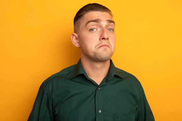 Jovem bonito de camisa verde sorrindo com expressão cética