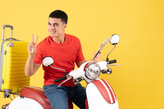 Jovem bonito de frente para o ciclomotor segurando o mapa fazendo sinal de vitória