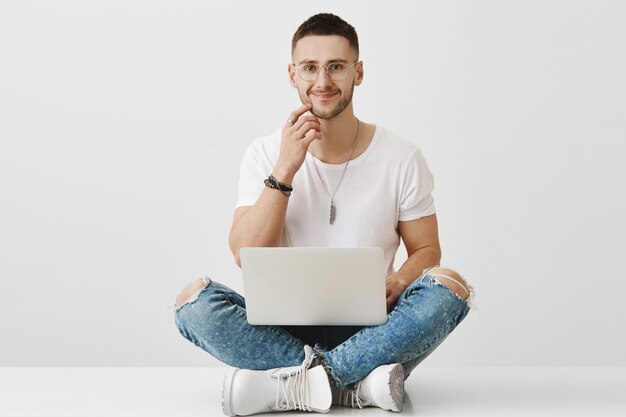 Jovem bonito de óculos posando com seu laptop