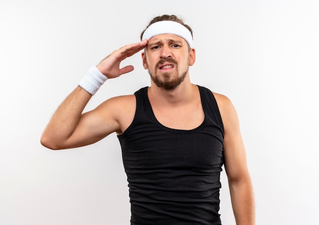 Jovem bonito e desportivo descontente usando bandana e pulseiras, colocando a mão perto da cabeça, parecendo isolado no espaço em branco