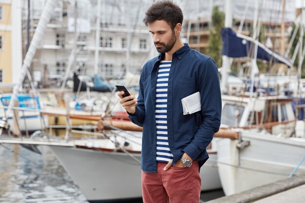 jovem bonito e sério de barba caminhando ao longo do porto