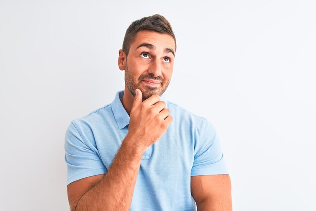 Jovem bonito elegante vestindo camiseta azul sobre fundo isolado com mão no queixo pensando em pergunta expressão pensativa sorrindo com cara pensativa conceito de dúvida