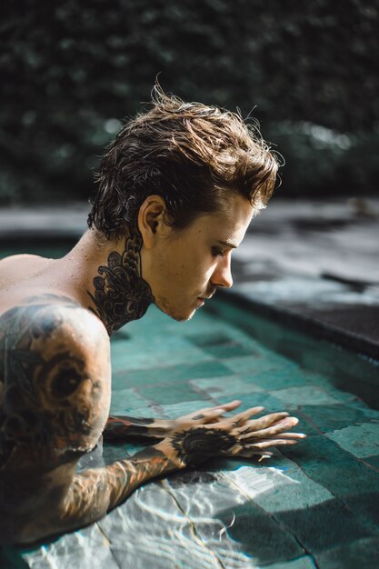 jovem bonito em tatuagens descansando na piscina ao ar livre.