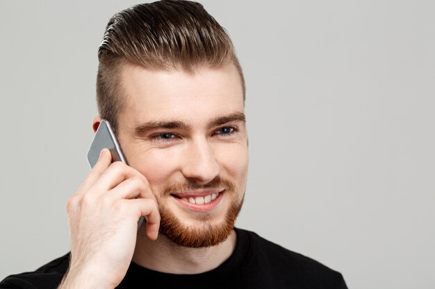 Jovem bonito falando no telefone sobre parede cinza.