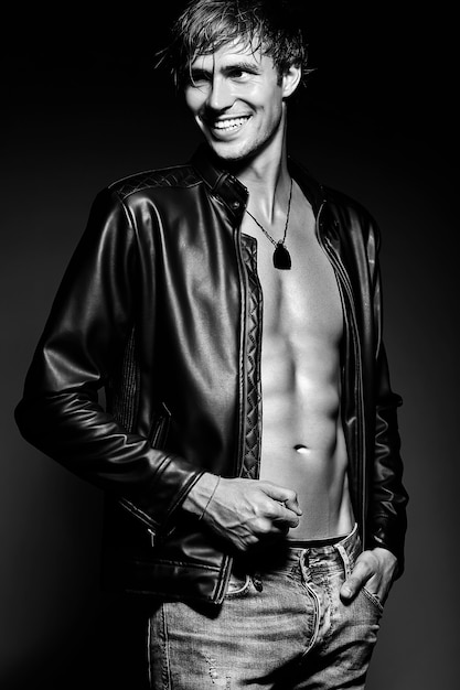 Jovem bonito musculoso cabe homem modelo masculino posando no estúdio, mostrando seus músculos abdominais na jaqueta de couro