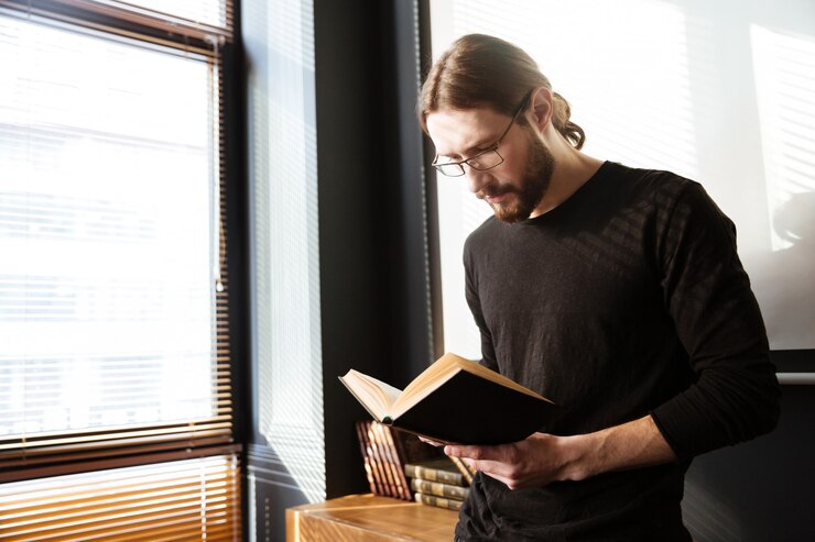 Foto grátis jovem bonito no escritório trabalhando enquanto lê o livro.