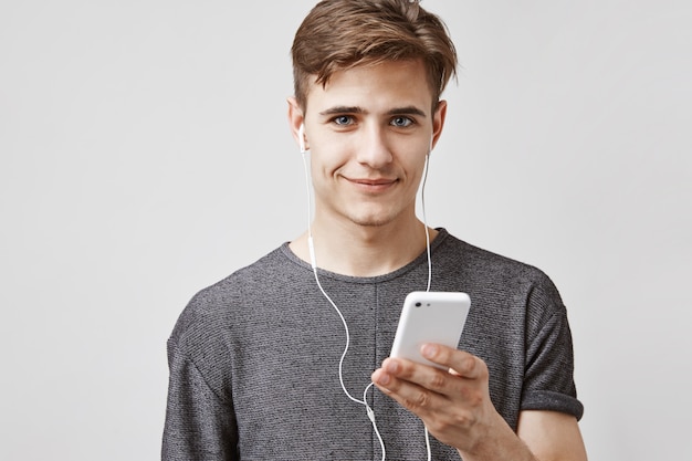 Jovem bonito ouve música no smartphone com fones de ouvido. aplicativo de música