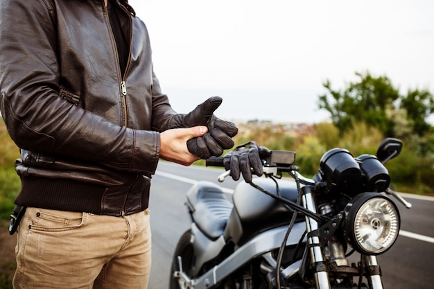 Jovem bonito posar perto de sua moto, usando luvas.