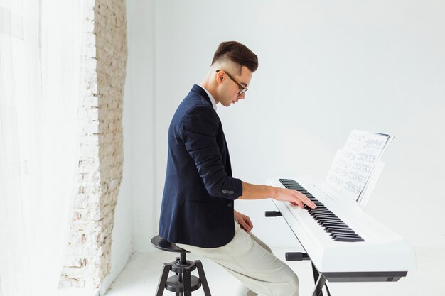 Jovem bonito praticando teclado de piano