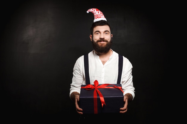 Jovem bonito segurando a caixa de presente de Natal sobre preto.