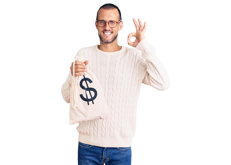 Foto grátis jovem bonito segurando o saco de dinheiro com o símbolo do dólar fazendo sinal de ok com os dedos sorrindo amigável gesticulando excelente símbolo