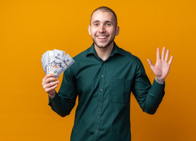 Jovem bonito sorridente com uma camisa verde segurando dinheiro e mostrando cinco