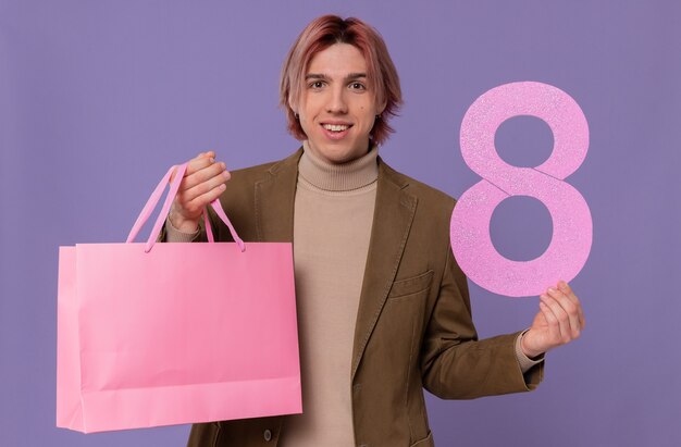 Jovem bonito sorridente segurando uma sacola de presente rosa e o número oito