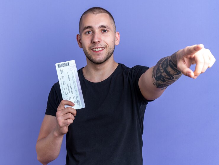 Foto grátis jovem bonito sorridente, vestindo uma camiseta preta segurando as bilheterias na frente, isoladas na parede azul