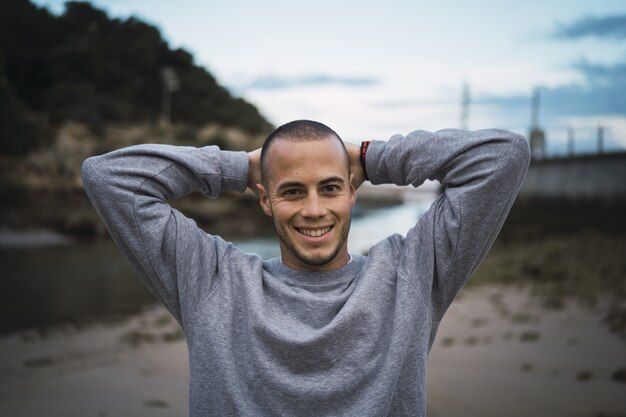 Jovem bonito sorrindo e posando com as mãos na cabeça