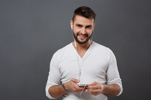 Jovem bonito sorrindo segurando o telefone sobre parede cinza