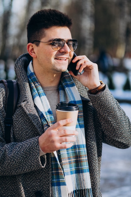 Jovem bonito tomando café fora e usando o telefone