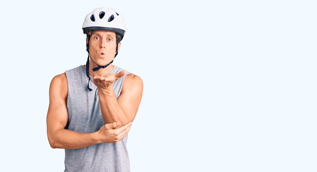 Foto grátis jovem bonito usando capacete de bicicleta, olhando para a câmera, mandando um beijo com a mão no ar, sendo uma expressão de amor adorável e sexy