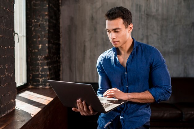 Jovem bonito usando laptop perto da janela