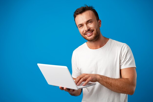 Jovem bonito usando seu laptop contra um fundo azul