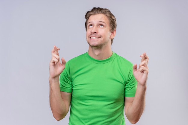 Foto grátis jovem bonito vestindo camiseta verde fazendo um desejo desejável cruzando a mão com uma expressão esperançosa