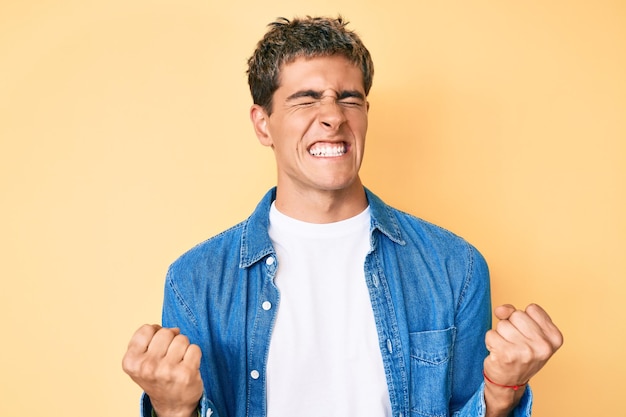 Foto grátis jovem bonito vestindo roupas casuais muito feliz e animado fazendo gesto vencedor com os braços levantados sorrindo e gritando para o conceito de celebração de sucesso