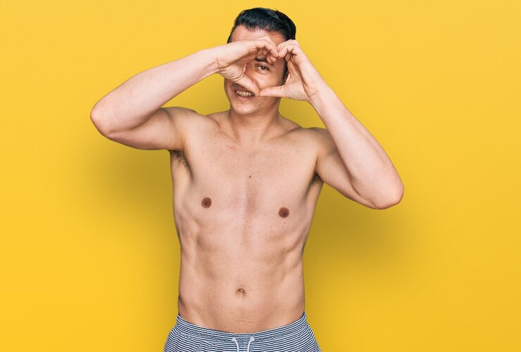 Foto grátis jovem bonito vestindo trajes de banho sem camisa fazendo forma de coração com a mão e os dedos sorrindo olhando através do sinal