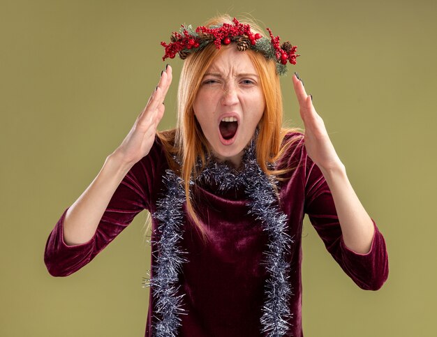 Jovem brava linda com um vestido vermelho com grinalda e guirlanda no pescoço isolado na parede verde oliva