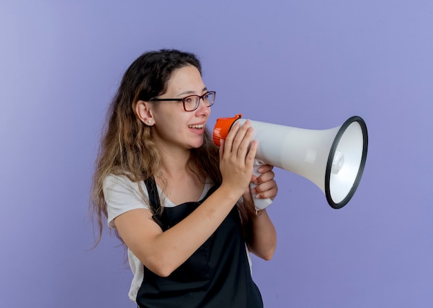 Jovem cabeleireira profissional de avental falando para o megafone e sorrindo alegremente