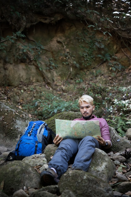 Jovem caminhante cansado com mochila sentada na rocha na floresta enquanto descansava após uma caminhada ativa. Conceito de viagem