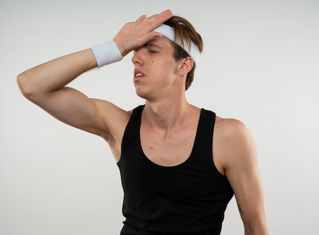 Foto grátis jovem cansado e esportivo usando bandana e pulseira, colocando a mão na testa isolada na parede branca