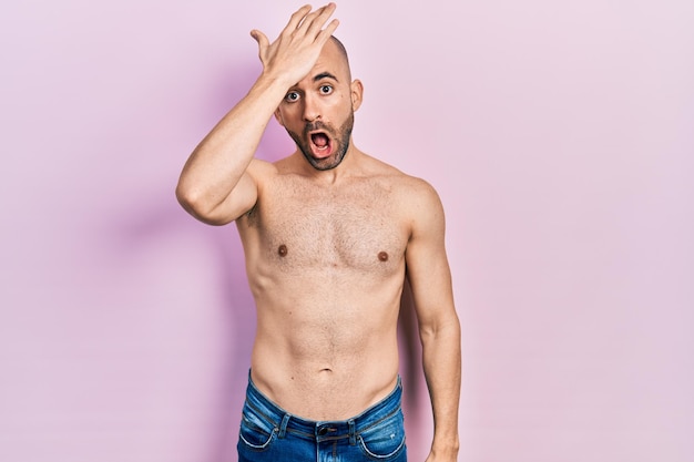 Foto grátis jovem careca em pé sem camisa surpreso com a mão na cabeça por engano lembre-se do erro esqueceu o conceito de memória ruim